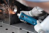 O persoană care poartă echipament de siguranță șlefuiește o muchie metalică cu o unealtă electrică, creând scântei.