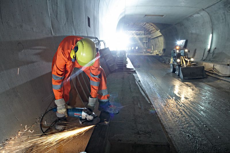 O persoană purtând echipament de siguranță șlefuiește metal pe un șantier, în interiorul unui tunel.