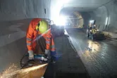 O persoană purtând echipament de siguranță șlefuiește metal pe un șantier, în interiorul unui tunel.