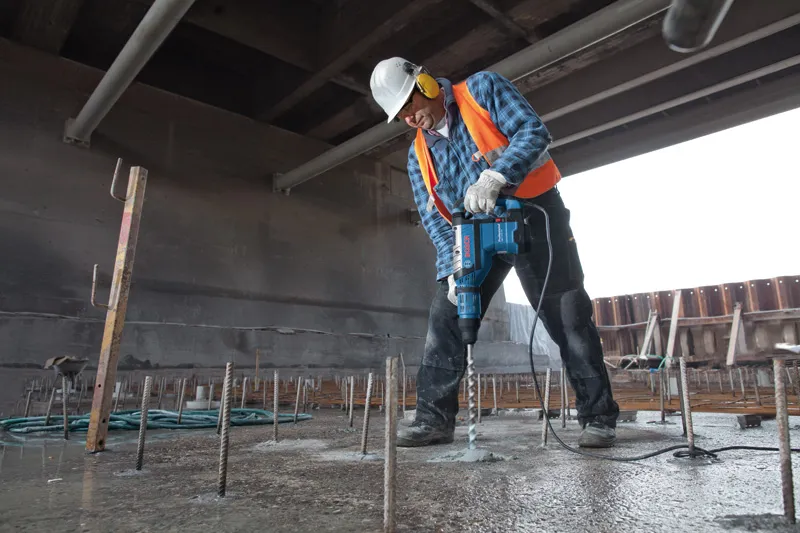 O persoană purtând echipament de siguranță găurește beton cu un ciocan rotopercutor.