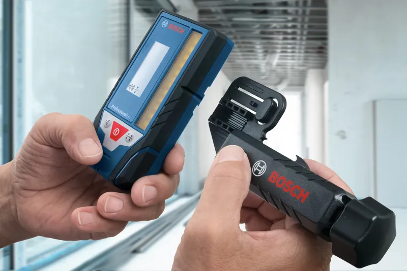 Особа која држи ласерски пријемник и носач за монтажу у модерном ентеријеру.