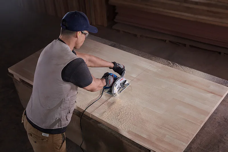 Особа која носи заштитну опрему сече дрво ручном кружном тестером.