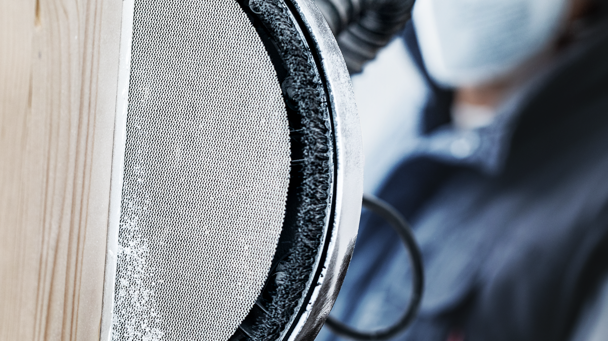 Особа која носи заштитну опрему брусила је дрвену површину електричним алатом.