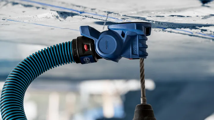 Прикључак за усисавање прашине повезан са бушилицом ствара рупу у бетонском плафону.