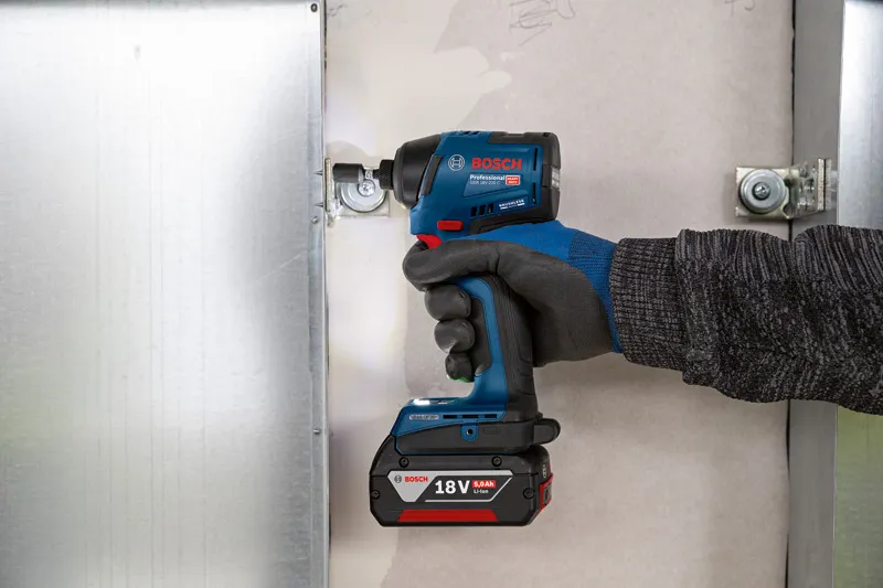 Особа која носи заштитну опрему користи акумулаторски ударни одвијач за причвршћивање металног оквира.