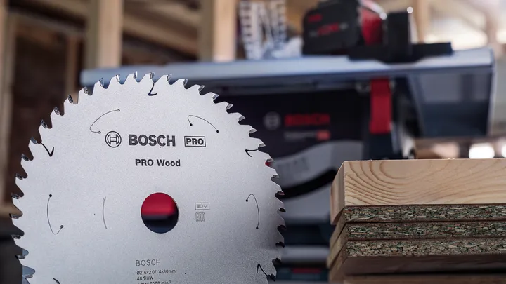 Сечиво кружне тестере испред наслаганих дрвених дасака у радионици.