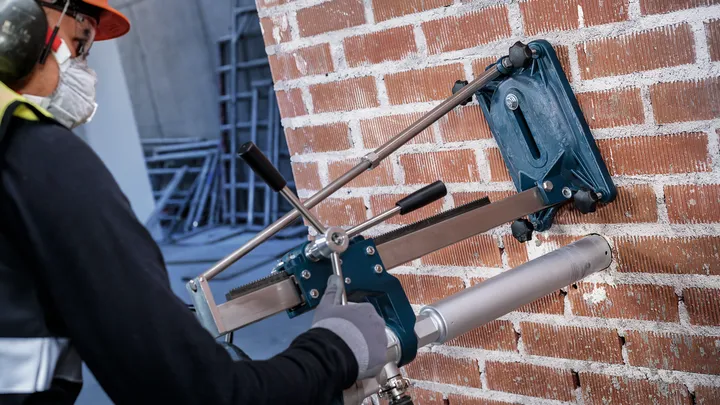 Особа која носи заштитну опрему буши велику рупу у зиду од цигле.