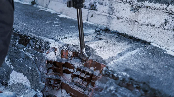 Алат за рушење разбија бетон на зиду од цигле.