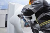 Особа која носи заштитну опрему бруси ивицу велике металне цеви напољу.