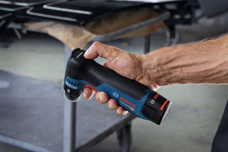 Особа држи акумулаторску брусилицу са случајном орбитом у радионичком окружењу.