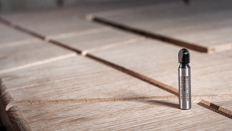 Метална глодала стоји усправно на жлебљеној дрвеној површини.