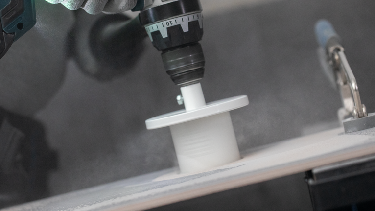 Особа која носи заштитну опрему буши кружну рупу у белој плочици.