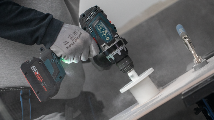 Особа која носи заштитну опрему буши рупу у белој површини.