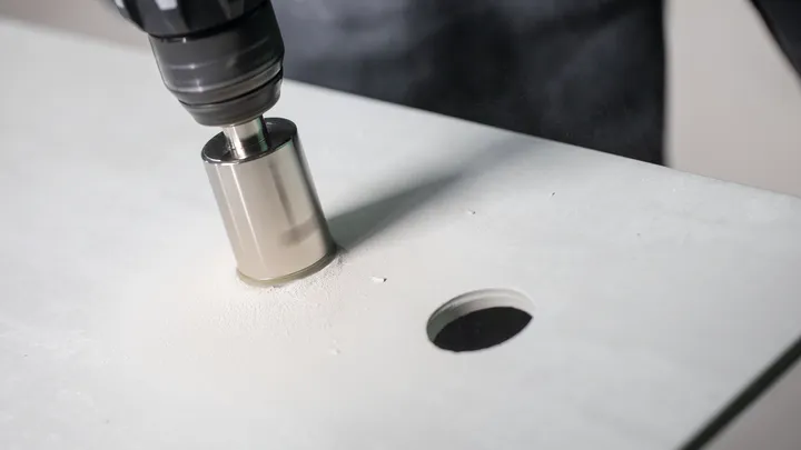 Кружна тестера буши кружну рупу у равној белој површини.