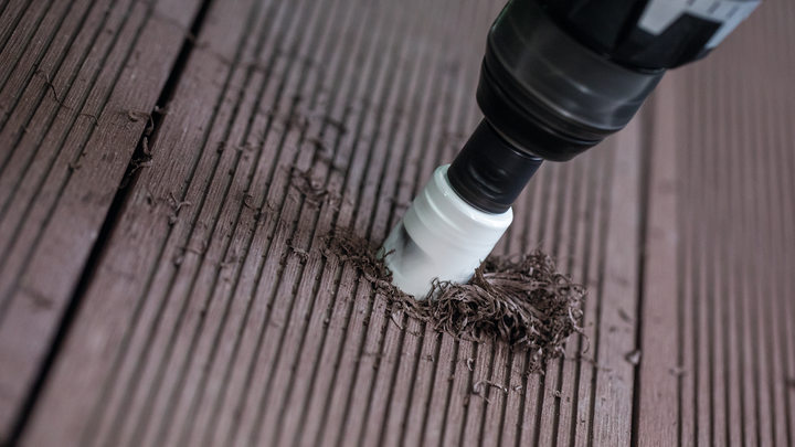 Електрични алат са наставком за кружну тестеру буши у дрвену површину палубе.