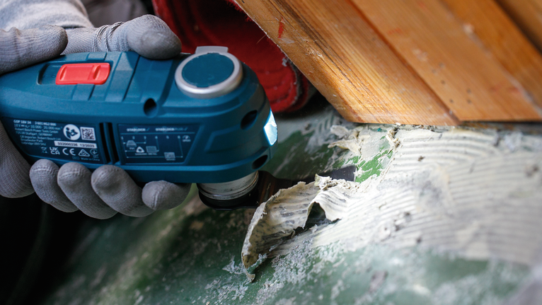 Особа која носи заштитну опрему уклања остатке лепка електричним алатом.