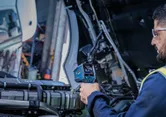 Особа која носи заштитну опрему користи термо детектор да провери мотор камиона.