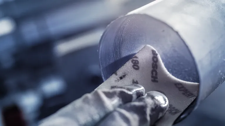 شخص يرتدي معدات السلامة يقوم بصنفرة الجزء الداخلي من الأنبوب المعدني.