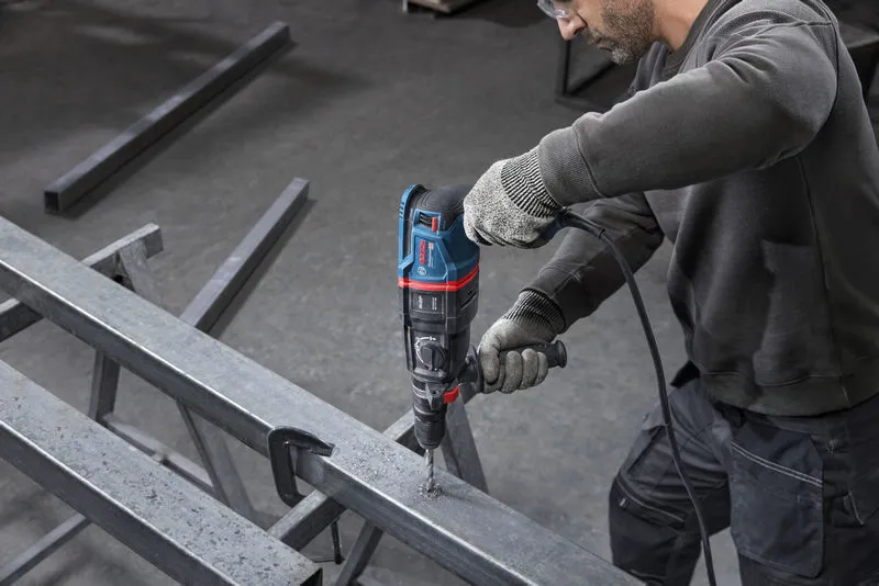 شخص يرتدي معدات السلامة يقوم بحفر شعاع معدني بمطرقة دوارة.