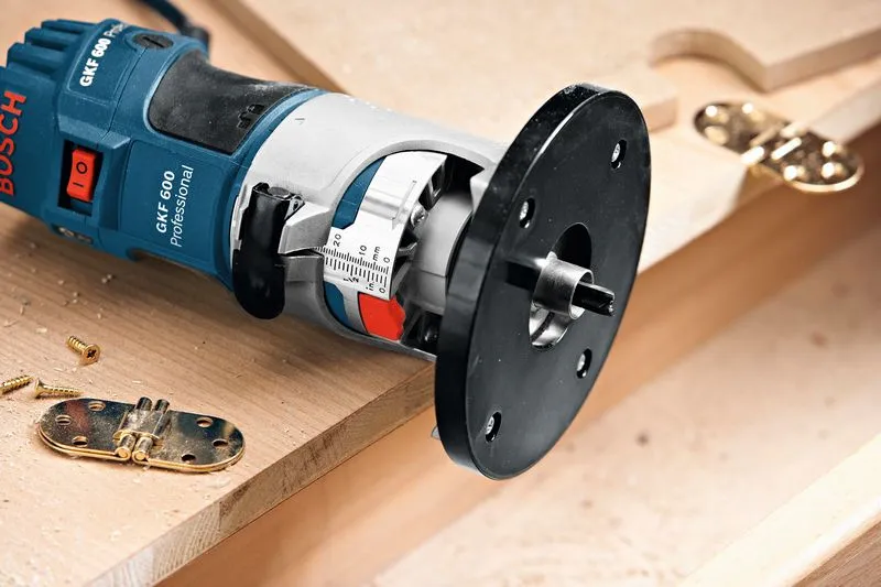 Palm router positioned near door hinges and screws on a wooden surface.