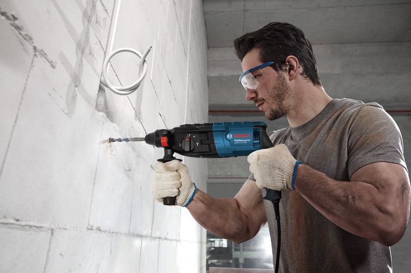 A person wearing safety equipment drills into a concrete wall with a power tool.