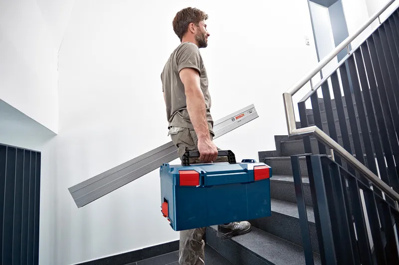 A person carries a tool case and an angle measurer while walking up stairs.