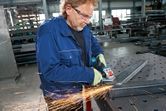 A person wearing safety equipment grinds metal with a cordless angle grinder.