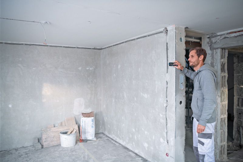 A person uses a laser measure to check wall distance at a construction site.