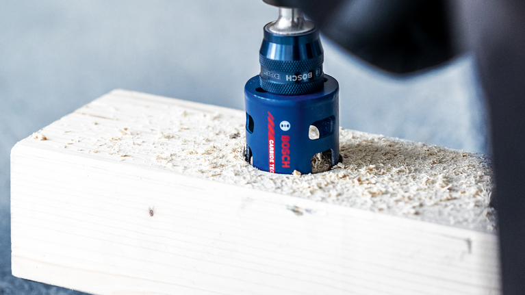 Hole saw drilling a round hole into a wooden plank.