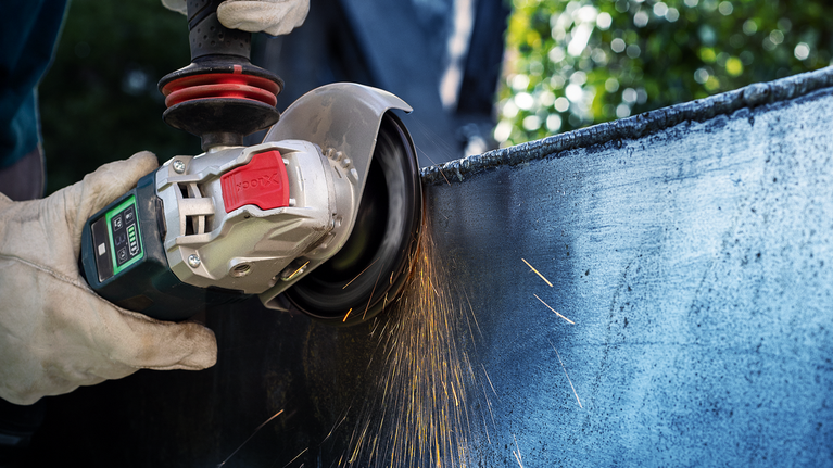 Person wearing safety equipment grinds metal, creating sparks.