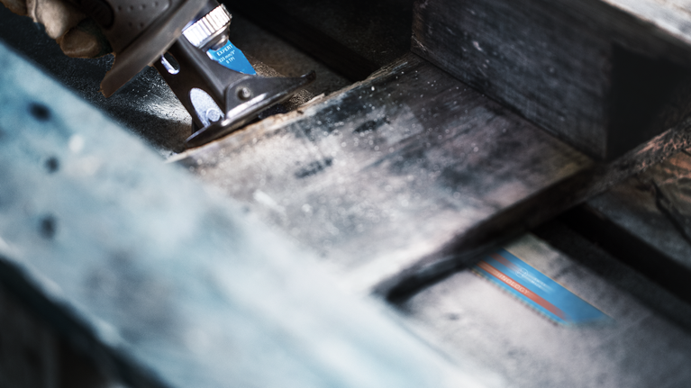 Person using a reciprocating saw to cut through a wooden beam.