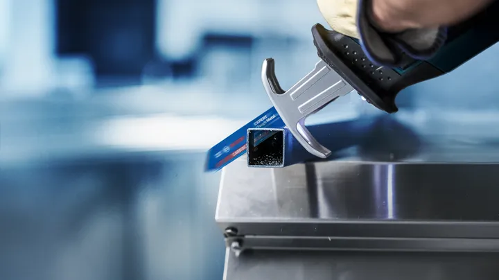 Person wearing safety equipment uses a reciprocating saw to cut a metal tube.