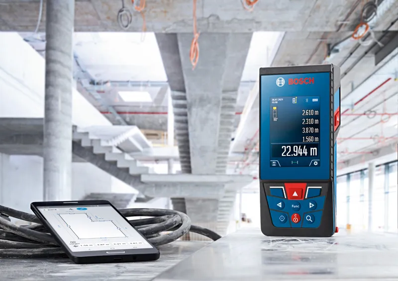 Laser measure with measurement display placed beside a tablet at a construction site.