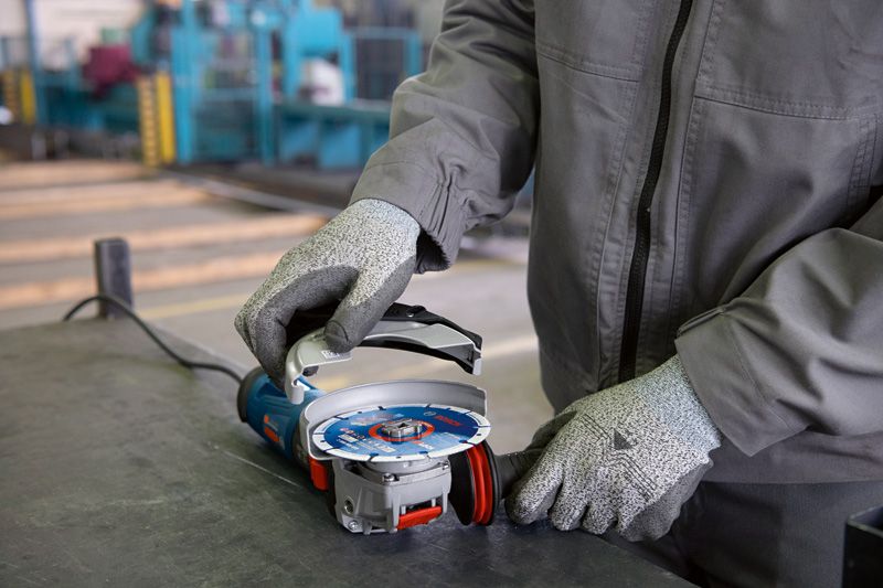 A person wearing safety equipment attaches a disc to an angle grinder on a workbench.