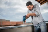 A person wearing safety equipment drills into a concrete ledge with an impact drill.
