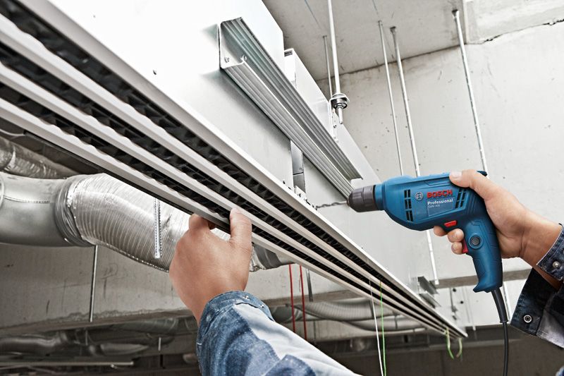 A person drills into a ceiling-mounted metal channel in an industrial setting.