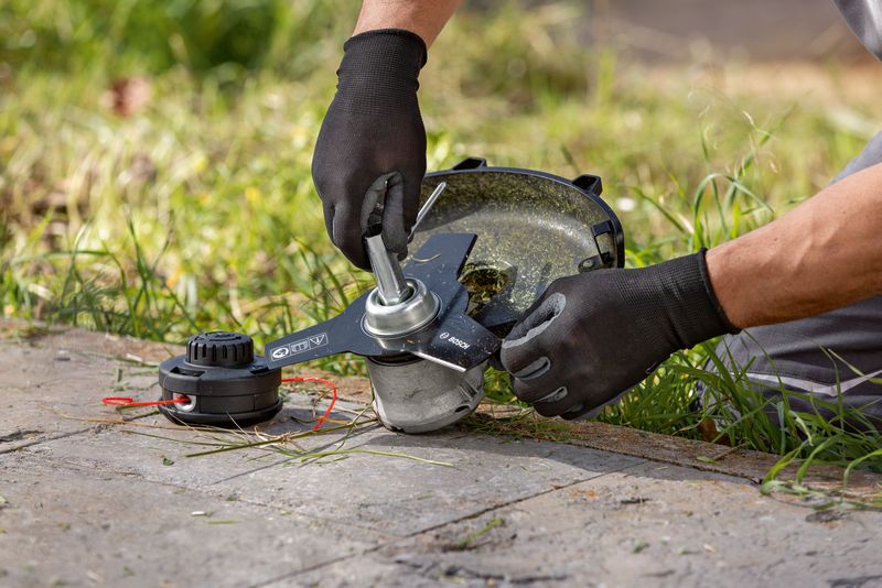 A person wearing safety equipment adjusts the head of a cordless brushcutter on grass.