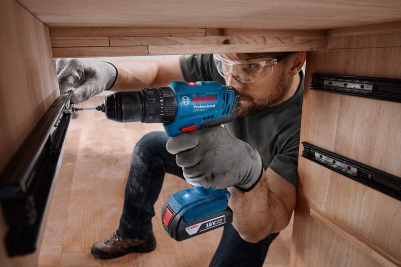 A person wearing safety equipment installs a drawer slide using a cordless drill.
