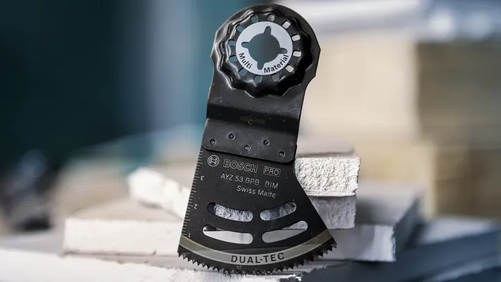 Oscillating multi-tool blade resting upright on stacked construction panels.