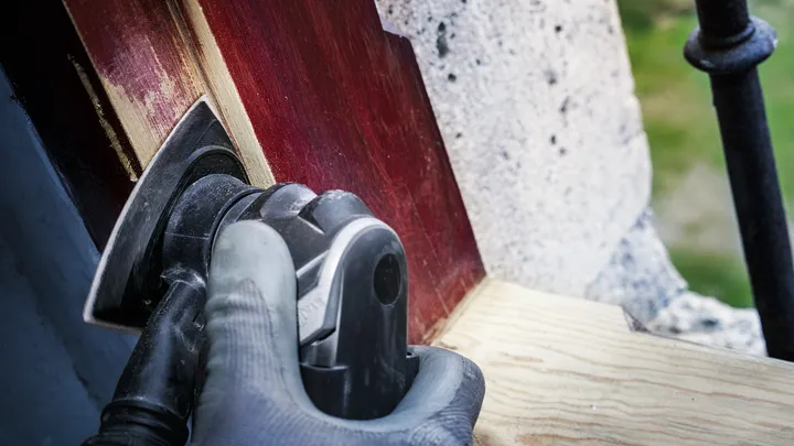 Person wearing safety equipment sanding painted wood with a power tool.