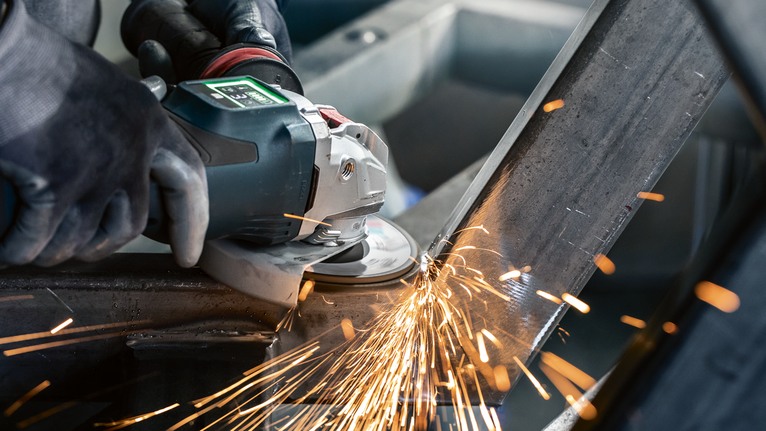 A person wearing safety equipment grinds metal, producing bright sparks.