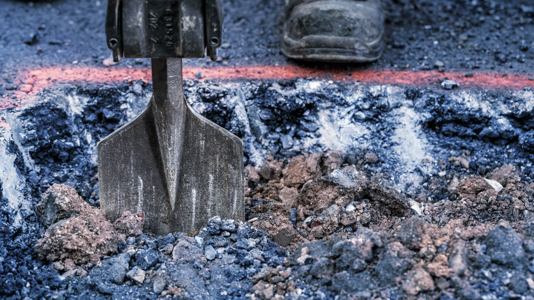Person using a demolition tool to break up asphalt on a construction site.