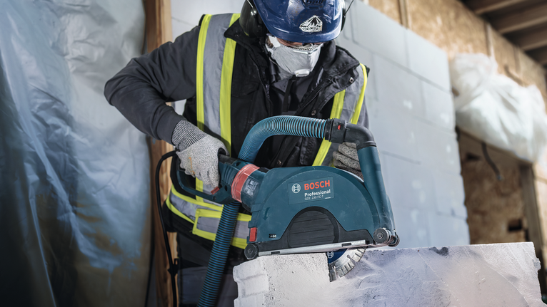 Person wearing safety equipment cuts a white stone block with a power tool.