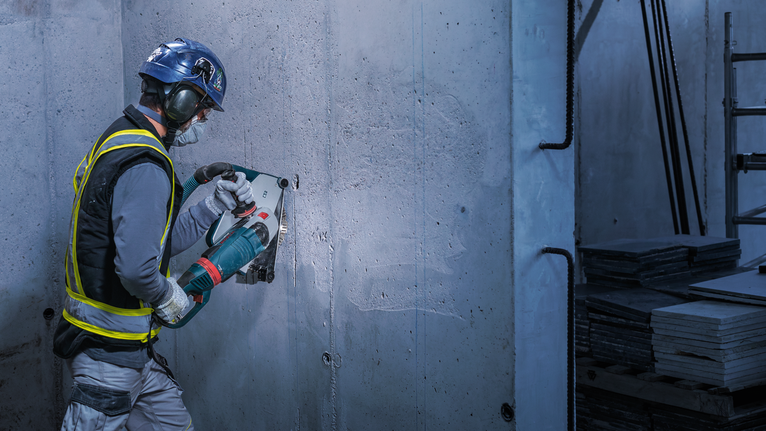 Worker wearing safety equipment cuts into a concrete wall with a large power tool.