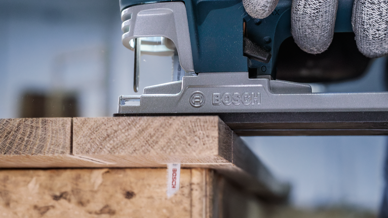 Person wearing safety equipment uses a jigsaw to cut a wooden board.