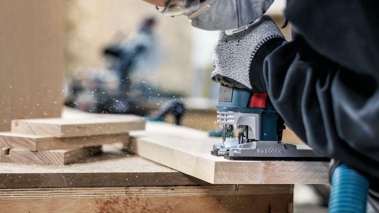 Person wearing safety equipment uses a jigsaw to cut wooden boards.