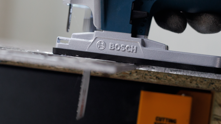 Person wearing safety equipment guides a jigsaw to cut through a wood board.