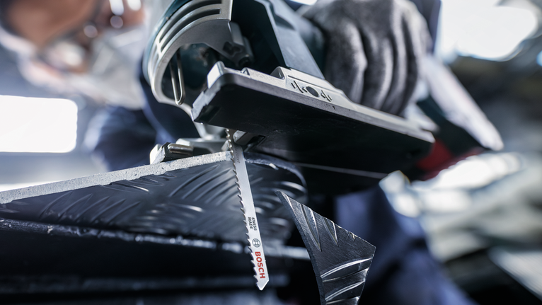 A person wearing safety equipment cuts patterned metal with a jigsaw.