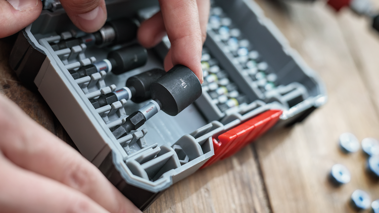 Person selecting a socket from a tool kit on a wooden workbench.