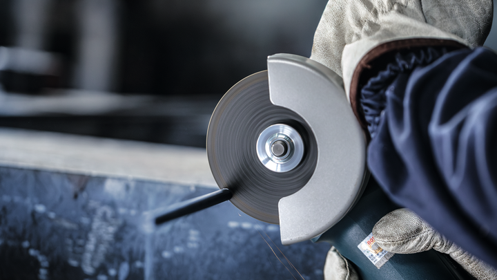 Person wearing safety equipment uses an angle grinder to cut metal.